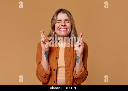 Eine fröhliche junge Frau lächelt breit und drückt ihre Finger in der Hoffnung auf Glück. Ihr stylisches Outfit bildet einen schönen Kontrast zu der warmen, sonnigen Ba Stockfoto