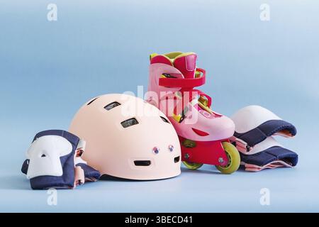 Set aus Rollschuhen und Schutzausrüstung - Knie-, Ellenbogen- und Handgelenkpolster und Helm in rosa Farben. Blauer Hintergrund, flache Lagen. Stockfoto