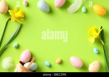 Happy Easter Grußkarte Vorlage. Rahmen aus bunten Ostereiern, Narzissen Frühlingsblumen auf grünem Hintergrund. Flach, Draufsicht, Kopierraum. Stockfoto
