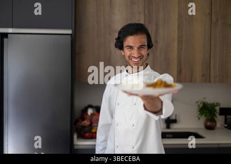 Professioneller Koch im weißen Mantel, der einen Teller Reis und Curry hält, lächelt in der Küche Stockfoto