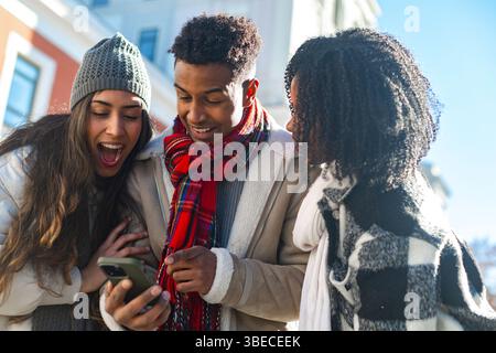 Gruppe fröhlicher, multiethnischer Freunde, die überrascht sind, während sie lustige Videos oder Fotos auf dem Mobiltelefon im Freien anschauen Stockfoto