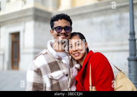 Junges, multiethnisches Paar lächelt und umgeht draußen in der städtischen Umgebung, zeigt Liebe, Glück und Zweisamkeit Stockfoto
