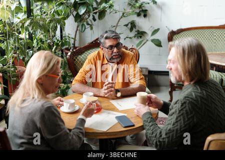 Drei Kollegen, die am Tisch sitzen und Kaffee genießen und sich in entspannter Atmosphäre mit Innenpflanzen unterhalten Stockfoto