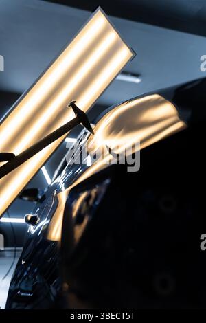 Der Techniker verwendet PDR-Werkzeuge, um Dellen von der Motorhaube während der lacklosen Reparatur der Dellen zu entfernen. Bei der lacklosen Dellen-Reparatur bei PDR werden Dellen unter hellen Stellen angestoßen Stockfoto