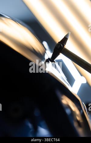 Der Techniker verwendet PDR-Werkzeuge, um Dellen von der Motorhaube während der lacklosen Reparatur der Dellen zu entfernen. Bei der lacklosen Dellen-Reparatur bei PDR werden Dellen unter hellen Stellen angestoßen Stockfoto