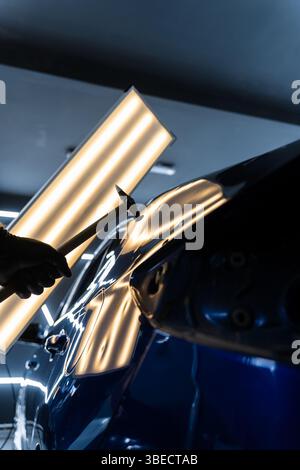Der Techniker verwendet PDR-Werkzeuge, um Dellen von der Motorhaube während der lacklosen Reparatur der Dellen zu entfernen. Bei der lacklosen Dellen-Reparatur bei PDR werden Dellen unter hellen Stellen angestoßen Stockfoto
