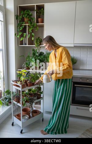Frau, die Topfpflanzen auf Tablett im Garten der Hausküche gießt. Pflanzenpflege, Gartenbau im Innenbereich Stockfoto