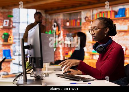 Programmierer im Startup-Büro, der ein großes Sprachmodell verwendet, um Hilfe beim Codierungsprojekt zu erhalten. afroamerikanischer Mitarbeiter, der mit KI LLM Chatbot PC GPT-Software auf PC am Arbeitsplatz für Softwareentwicklung interagiert Stockfoto