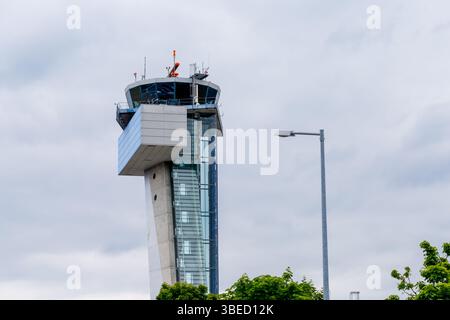 Nürnberg, Deutschland - 25. Mai 2025: Bild zeigt einen Flughafenkontrollturm vor bewölktem Himmel, mit einer nahen Straßenlaterne und grünem Laub am B Stockfoto