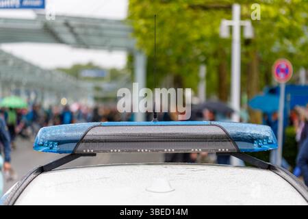 Nürnberg, Deutschland - 25. Mai 2025: Nahaufnahme eines Polizeiwagendachs mit blauem Lichtbalken. Regentropfen sind sichtbar. Verschwommene Menge im Hintergrund. Stockfoto