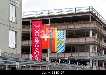 Nürnberg, Deutschland - 25. Mai 2025: Vier Fahnen stehen vor einem Gebäude und einem mehrstöckigen Parkhaus mit sichtbarer Vegetation. Stockfoto