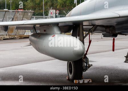 Nürnberg, Deutschland - 25. Mai 2025: Nahaufnahme des Flügels, des Fahrwerks und des externen Kraftstofftanks eines grauen Militärflugzeugs auf nassem Untergrund. Stockfoto