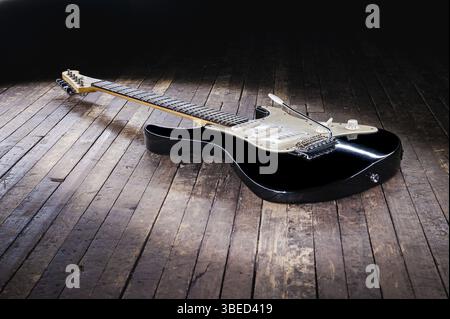 Schwarz-weiße E-Gitarre mit gelbem Stempel liegt auf einer Holzbühne Stockfoto