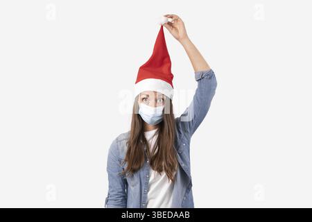Junge Frau mit Telefon medizinische Maske und santa Hut. Weihnachtseinkäufe online auf Quarantäne. Stockfoto