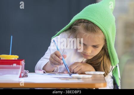 Mädchen malt mit Begeisterung Aquarelle, sitzen an einem Tisch im Hof Stockfoto