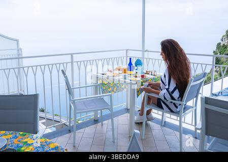 Frau, die auf einem Balkon mit Blick auf das Tyrrhenische Meer an der Amalfiküste speist Stockfoto