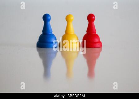 Drei Spielfiguren in Blau, Gelb und Rot, die hintereinander angeordnet sind und die Flaggenfarben von Rumänien, Moldawien, Andorra oder Tschad symbolisieren. Reflektiert auf einem Hochglanz Stockfoto