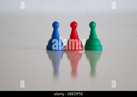 Drei Spielfiguren in Blau, Rot und Grün, symbolisch angeordnet, um die Farben der aserbaidschanischen Nationalflagge zu reflektieren, mit sanfter Reflexion. Stockfoto