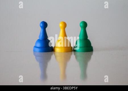 Drei Spielfiguren in Blau, Gelb und Grün, die die Nationalfarben Ruandas repräsentieren. Ein symbolisches und minimalistisches visuelles Konzept auf einem weißen s Stockfoto