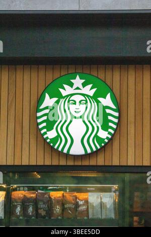 Starbucks-Logo auf einer Holzfassade eines Coffee-Shops. Verschiedene Kaffeebeutel sind unten auf dem Display zu sehen. Stockfoto