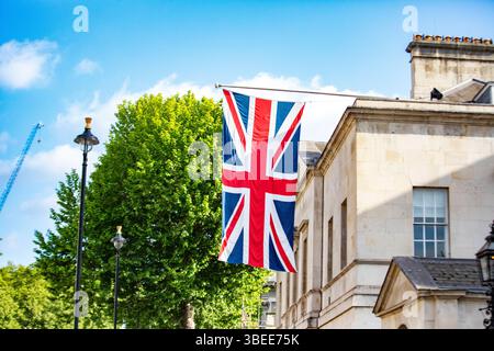 Die Union Jack Flagge fliegt stolz auf einem historischen Gebäude in London, Großbritannien. Hellblauer Himmel und üppig grüne Bäume ergänzen die Szene. Stockfoto
