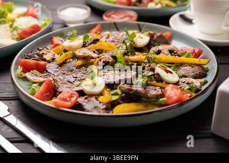 Salat mit gegrilltem Rindfleisch, Pfeffer, Kirschtomaten und Wachteleiern, serviert auf einem Holztisch im Restaurant Stockfoto