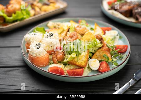 Nahaufnahme von Meeresfrüchten Caesar Salat mit Garnelen, Sushi-Brötchen, Lachs, Frischkäse, Kirschtomaten und Salat auf Teller, die im Restaurant auf den Tisch gestellt werden. Er Stockfoto