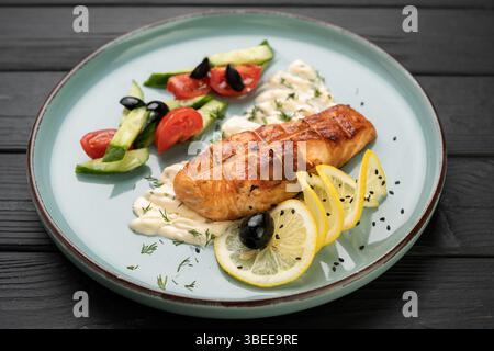 Gegrilltes Lachsfilet mit frischem Gemüse, cremiger Sauce und Zitrone auf Teller. Konzept der Meeresfrüchte Restaurant Menü, gesunde Gourmet Fisch Gericht mit Stockfoto