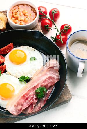 Frühstück in der Pfanne mit Spiegeleiern, Speck, Tomaten, Bohnen, Toast auf weißem Hintergrund. Draufsicht. Stockfoto