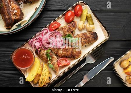 Gegrillter lula-Kebab aus traditioneller türkischer Küche. Serviert mit goldenen Kartoffelscheiben, eingelegten Zwiebeln, gegrilltem Gemüse, frischen Tomaten und Ketchup Stockfoto