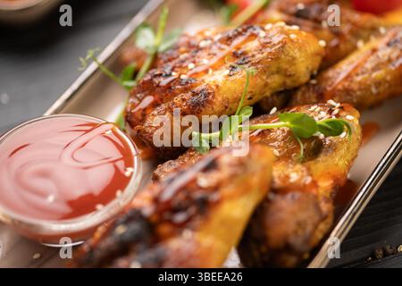 Knusprig gegrillte Hähnchenflügel mit Ketchup und Tomaten auf weißem Gericht auf hölzernem Hintergrund. Konzept von hausgemachtem Mittagessen, Barbecue-Stil, rustikalen ta Stockfoto