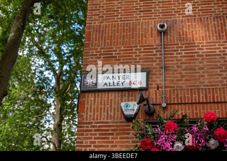 Ziegelmauer mit Straßenschild für die Panyer Alley in London. Blumenanordnung und CCTV-Kamera ebenfalls sichtbar. Stockfoto
