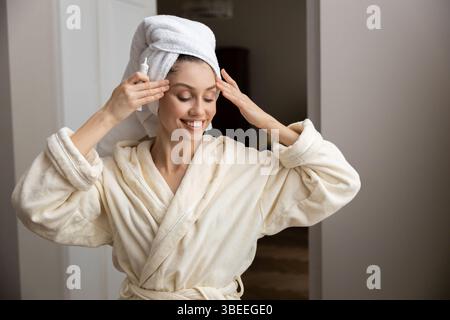 Frau mit einem Handtuch um den Kopf gewickelt und sanft Creme auf die Haut aufgetragen Stockfoto