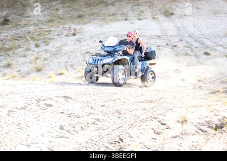 moskau, russland, 26.08.2016 Ein Mann fährt mit einem Vierrad auf einer Sandstraße. Der Mann trägt einen roten Hut und eine Sonnenbrille Stockfoto