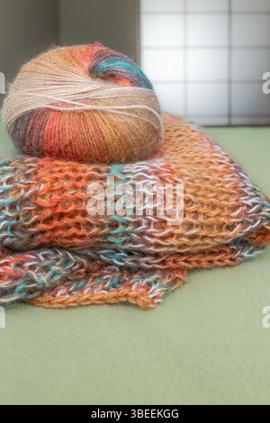 Farbenfrohe Strickjacke aus Mohair in warmen Farben mit einem Knäuel Garn. Strickmode. Herbst- und Wintergarderobe. Gemütliches Zuhause. Warme Sachen. Handwerkliches Produkt Stockfoto