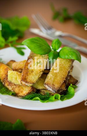 Hausgemachte gebratene Zucchini auf einem weißen Teller auf braunem Hintergrund. Stockfoto