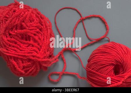 Zwei rote Fäden in Form eines Herzens. Rotes Garn. Herzform. Rot und grau. Handwerker. Strickstil. Stricken oder häkeln. Wort oder Symbol aus Garn Stockfoto