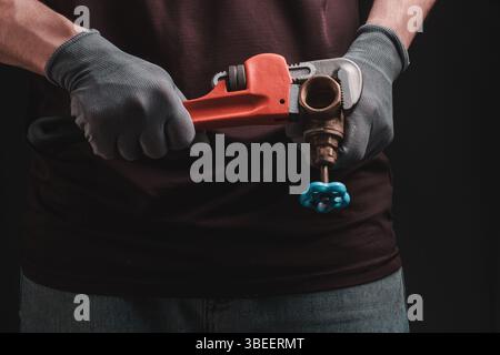 Klempner mit Affenschlüssel und Flügelhahn in der Hand auf dunklem Hintergrund Stockfoto