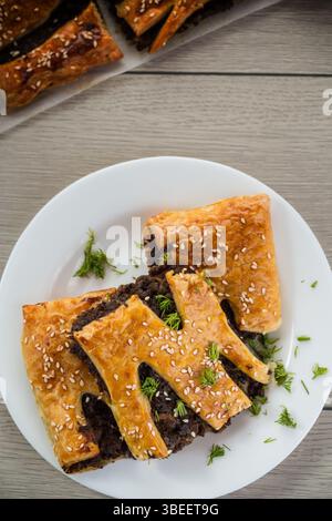 Goldenes Blättergebäck mit Pilzfüllung und Sesamsamen auf einem hellen Holztisch. Stockfoto
