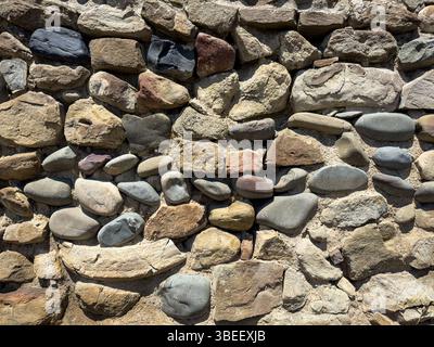 Nahaufnahme einer rustikalen Steinmauer aus natürlichen unregelmäßigen Felsen, verschiedenen Farben und Texturen, rauer Oberfläche, Tageslicht, abstraktem Hintergrund. Keine Personen. Stockfoto