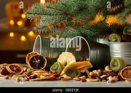Getrocknete tropische Früchte mit verschiedenen Nüssen und Rosinen in kleinen Metalleimern. Süße tropische Früchte und Weihnachtsbaum auf einem Küchentisch. Stockfoto