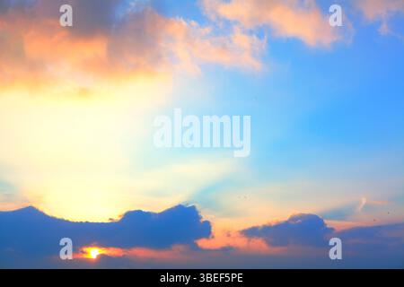 Der Himmel ist mit atemberaubenden Farben bemalt, während die Sonne hinter einer Wolkenbildung untergeht. Kontrast zwischen beleuchteten Wolkenrändern und schattierten Kanten Stockfoto