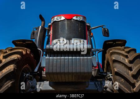 Blick von unten auf den großen Traktor mit riesigen Rädern auf dem Feld gegen den Himmel. Stockfoto
