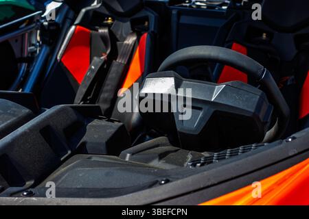 Nahaufnahme eines schwarzen Lenkrads und orangefarbene Sitze in einem Fahrzeug an einem sonnigen Tag. Stockfoto