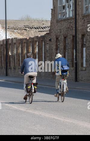 Zwei Personen fahren eine Straße hinunter mit dem Fahrrad, möglicherweise zur Freizeit oder zum Sport, vor einem Backsteinhaus. Stockfoto