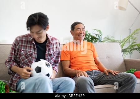 Fröhlicher Familienmoment. Vater und Sohn teilen ein unbeschwertes Erlebnis, während sie zu Hause ein Fußballspiel beobachten. Stockfoto