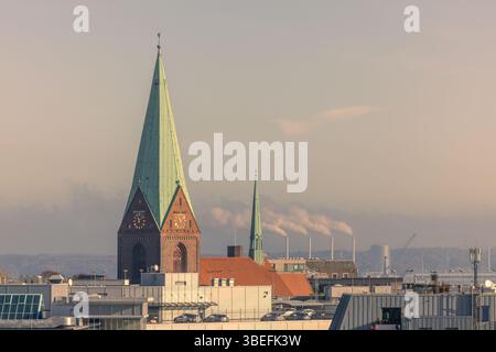 Blick von der Dachterrasse auf Kiel, Deutschland, mit dem zentralen Kirchturm in warmem Licht und entfernten Schornsteinen im Hintergrund. Nur redaktionelle Verwendung. Stockfoto