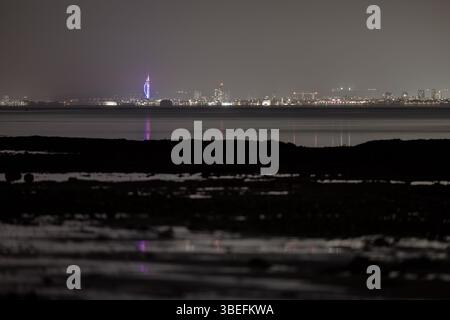 Blick auf die Skyline von Portsmouth und den Spinnaker Tower bei Nacht von der Isle of Wight, mit Reflexionen im ruhigen Wasser des Solent. Stockfoto