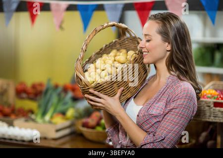 Frau, die Korbkorb mit gelben Kartoffeln auf dem Markt mit Tomaten und Flaggen hält Stockfoto