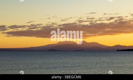 Sonnenuntergang über Lake Taupo, Neuseeland. Am Horizont befinden sich die vulkanischen Gipfel des Tongariro-Nationalparks: Ruapehu, Tongariro und Ngauruhoe Stockfoto